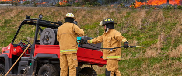 Fireman wearing Lakeland fire gear using equipment to extinguish a brush fire.