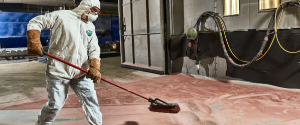 Worker wearing Safegard Economy Coverall and mask and goggles while sweeping dry material on floor of warehouse.